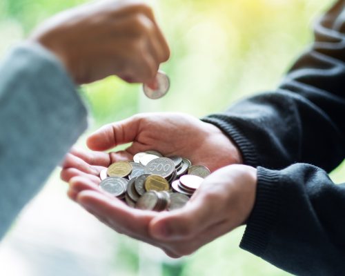 Closeup image of a hand putting coins into another people's hands